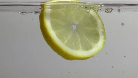 Macro slow motion of fresh slice of lemon thrown into a glass of cold water. Stock Footage 104404368