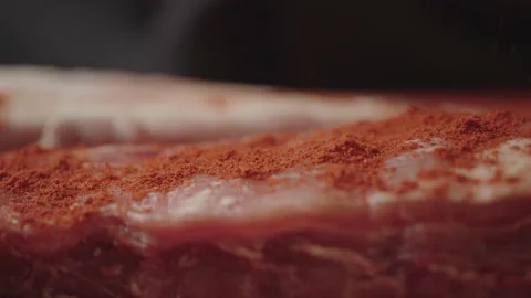 Macro slow motion video of chef sprinkling red pepper on meat in kitchen Stock Footage 233614137