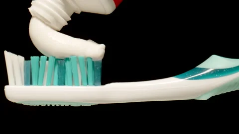 MACRO: Squeezing toothpaste from a tube onto a toothbrush on a black background Stock Footage 168682093