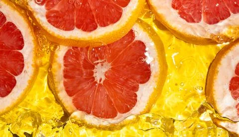 Macro texture of pink grapefruit slices in liquid with bubbles and waves Stock Photos