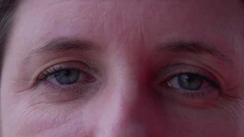 Macro tight close up of a woman in 40s with blue eyes looking at camera. Fe