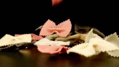 MACRO: Uncooked bow tie pasta fall on a black table, Slow motion Stock Footage 181799098