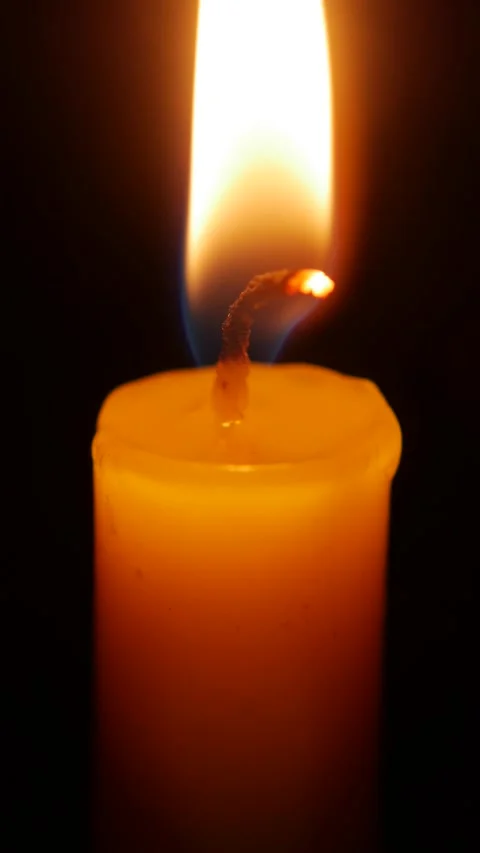 A macro vertical shot captures a candle flame rising against deep blackness Video stock 325034924