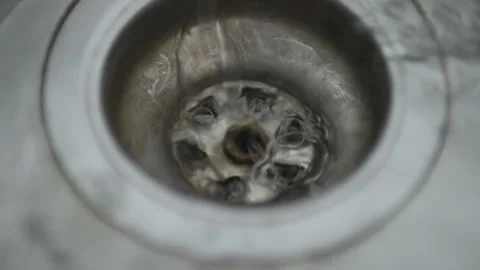 Macro view from above of clear water spiraling down into a metal sink drain. Stock Footage 327159101