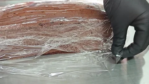Macro view of a baker wrapping chocolate cake in transparent plastic film. Stock-Footage 346472413