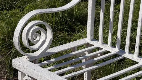 Macro view of a decorative spiral armrest on a white metal park bench against a Stock Photos