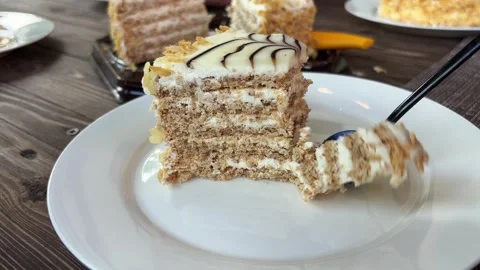 Macro view of a dessert spoon breaking a soft delicate slice of layer cake Stock Footage 340770864