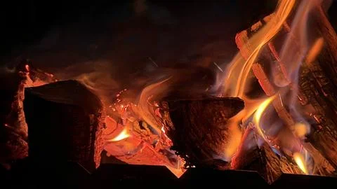 Macro view of glowing red-hot coals and vibrant fire consuming chopped firewood. Stock Photos
