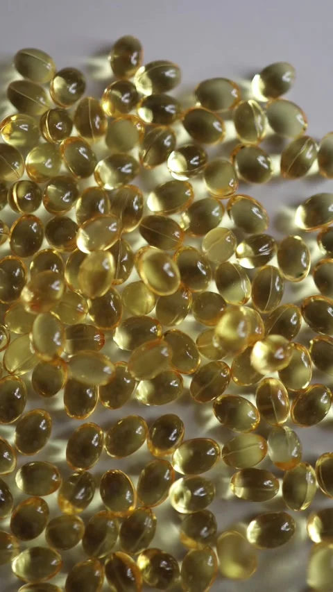 Macro view of golden vitamin D softgel capsules scattered on white surface Vidéo 342610168