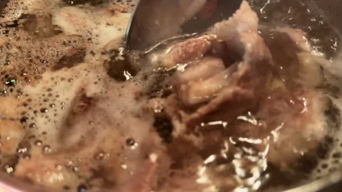 Macro view meat broth with foam and pieces of pork boiling in pan. POV stirring Stock Footage 267705016
