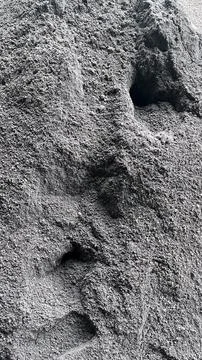 Macro view shows textured gray sand with multiple shallow footprints and irre Foto stock