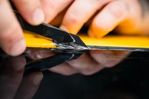 Macro view of technician trimming paint protection film on yellow car Stock Photos