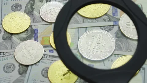Macro view through a magnifying glass on a bitcoin coins on a table with dollars Stock Footage 198677514