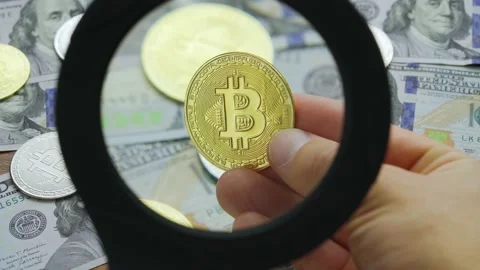 Macro view through magnifying glass on gold bitcoin coins on table with dollars Stock Footage 201184876