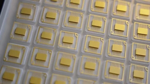 Macro view of a tray filled with gold-plated microchip carriers arranged in a Video stock 325976448