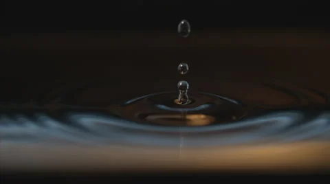 Macro water drop falls in slo-mo to water, splashing perfect concentric ripples Video stock 63825217