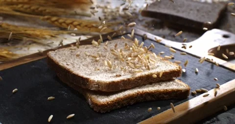 Macro of wheat grain seeds falling on fresh cereal bread on wooden cut board Stock Footage 268805135