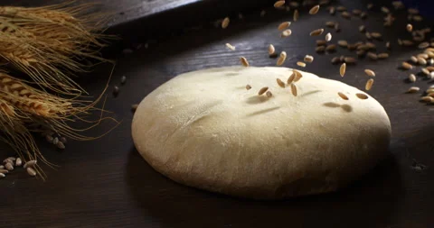 Macro of wheat grain seeds falling on raw loaf of dough on table in bakery Stock Footage 268806973