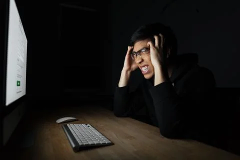 Mad irritated man working with computer in dark room Stock Photos