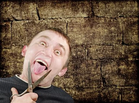 Mad man with scissors cuts off itself tongue on grunge background. Stock Photos
