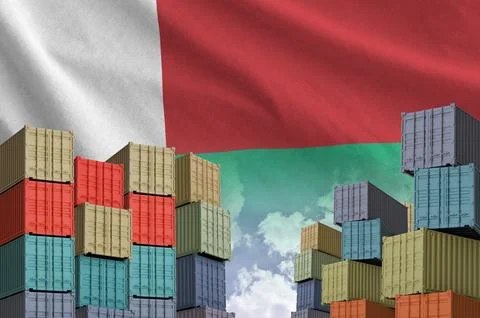 Madagascar flag and big stack of shipping cargo containers in docks with sky Stock Photos