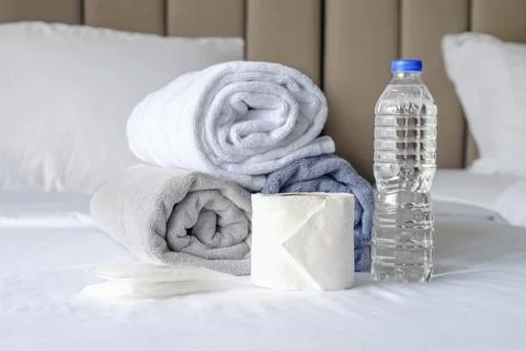 On the made bed are three towels folded into rolls, a bottle of drinking wate Stock Photos