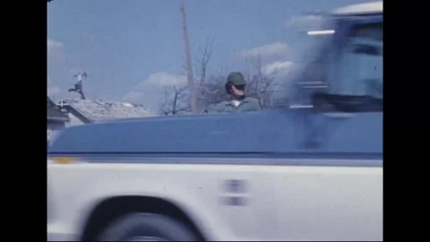 MADISON - 1974: Tornado Aftermath — Sunglassed soldier waves red car past Stock Footage 342230325