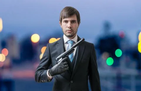 Mafia man or racketeer with pistol with silencer in hand at dusk. Stock Photos