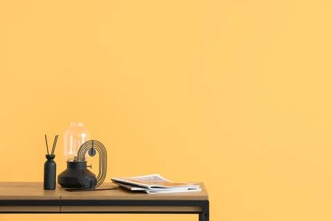 Magazines, lamp and reed diffuser on coffee table near orange wall in living  Stock Photos