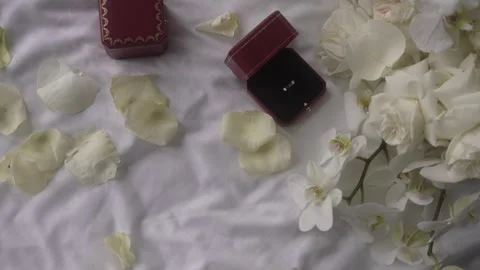 A magenta wedding ring rests on a bed near a bouquet of white flower petals Vidéo 265570493