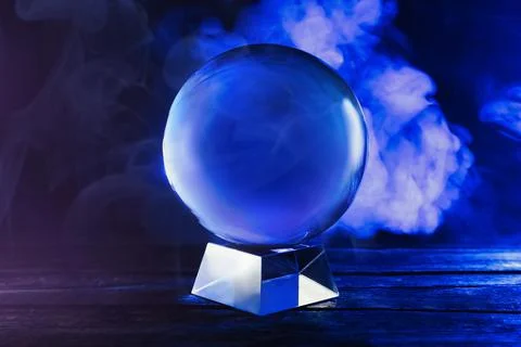Magic crystal ball on wooden table and smoke against dark background. Making  Stock Photos