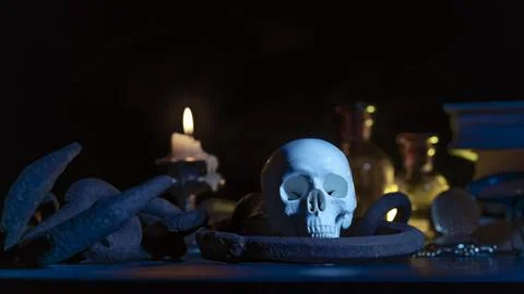 A magic skull on a wooden table, a burning candle in chains and a clock that has Stock Photos
