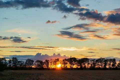 Magic sunset with sun low over the trees and dramatic clouds illuminated by l 스톡 사진
