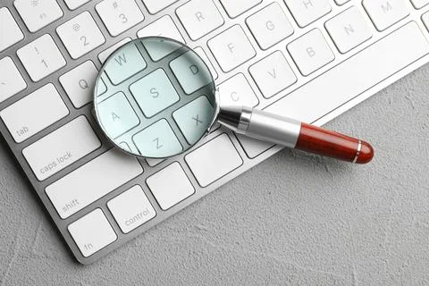 Magnifier glass and keyboard on light grey stone background, top view. Find k Stock Photos