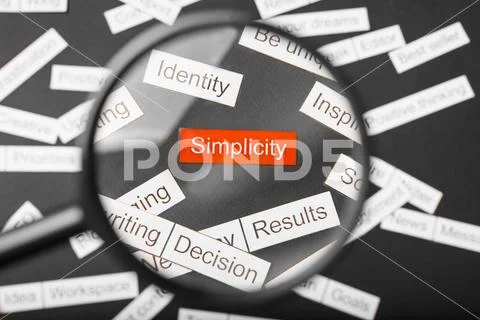 Magnifier glass over the red inscription simplicity cut out of paper. Surroun Stock Photos