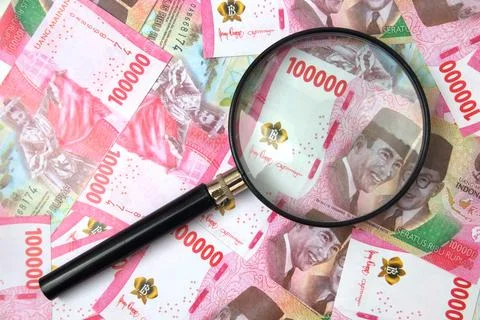 Magnifying glass above a stack of 100,000 rupiah bills Stock Photos