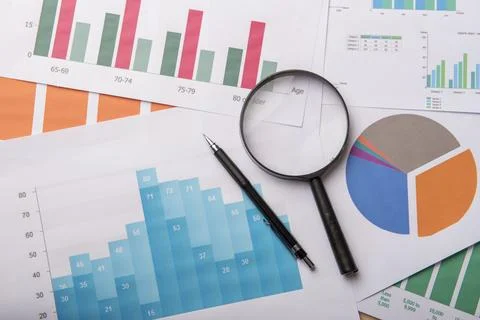 Magnifying glass and documents with analytics data lying on wood table Stock Photos