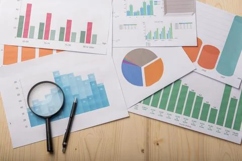 Magnifying glass and documents with analytics data lying on wood table Stock Photos