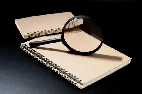 Magnifying glass and notebook on black background, investigate concept Stock Photos