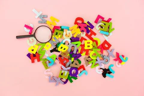 Magnifying glass with colorful alphabet on pink black background. Education c Stock Photos