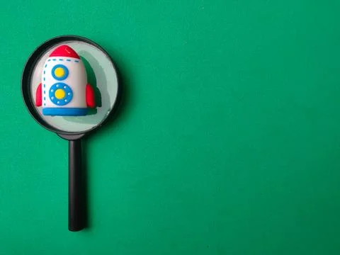 A magnifying glass frames a small toy rocket ship placed on the left side o.. Stock Photos