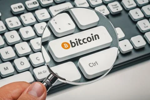 Magnifying glass in hand focused on computer key with bitcoin logo Stock Illustration