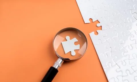Magnifying glass highlights a missing puzzle piece on orange background. Bu.. Stock Photos