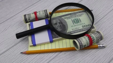 A magnifying glass lies on a bundle of 100 dollar bills with stationery Vídeos de archivo 147290948