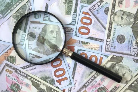 Magnifying glass over stack of 100 dollar bills Stock Photos