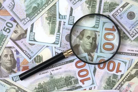 Magnifying glass over stack of 100 dollar bills Stock Photos