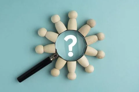 Magnifying glass with a question mark surrounded by wooden peg dolls on a b.. Photos