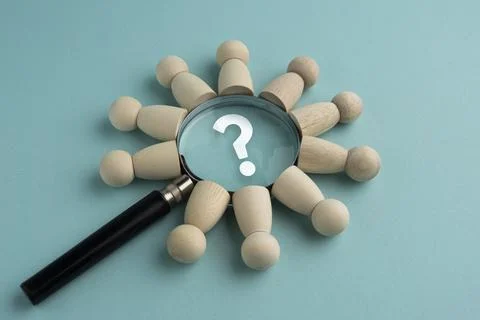 Magnifying glass with a question mark surrounded by wooden peg dolls on a b.. Stock Photos