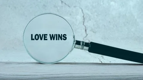A magnifying glass rests on a light table, enlarging the phrase Love Wins a.. Stock Photos