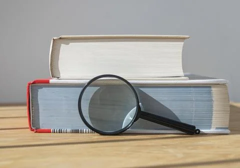Magnifying glass with stack of close thick books on wooden table with day lig Foto stock